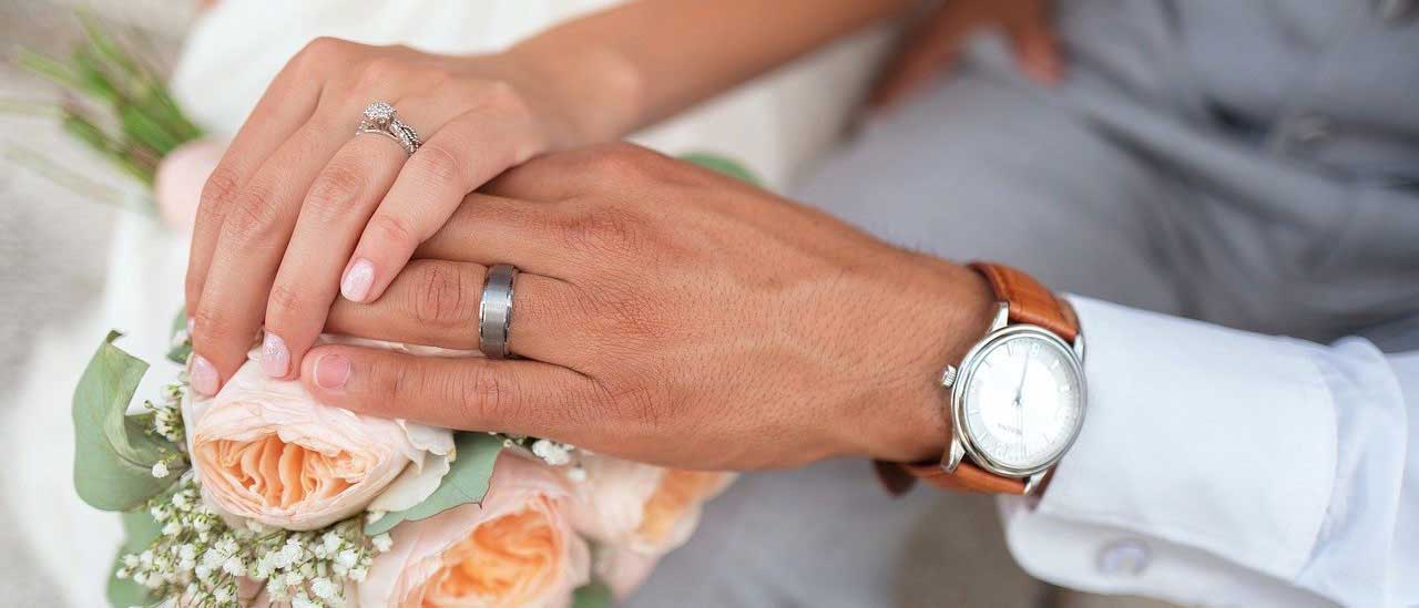 Photo of bride and groom's hands together over flower bouquet